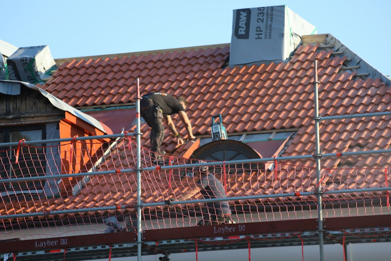 Couvreur au travail sur une toiture en tuiles, chantier sous échafaudage